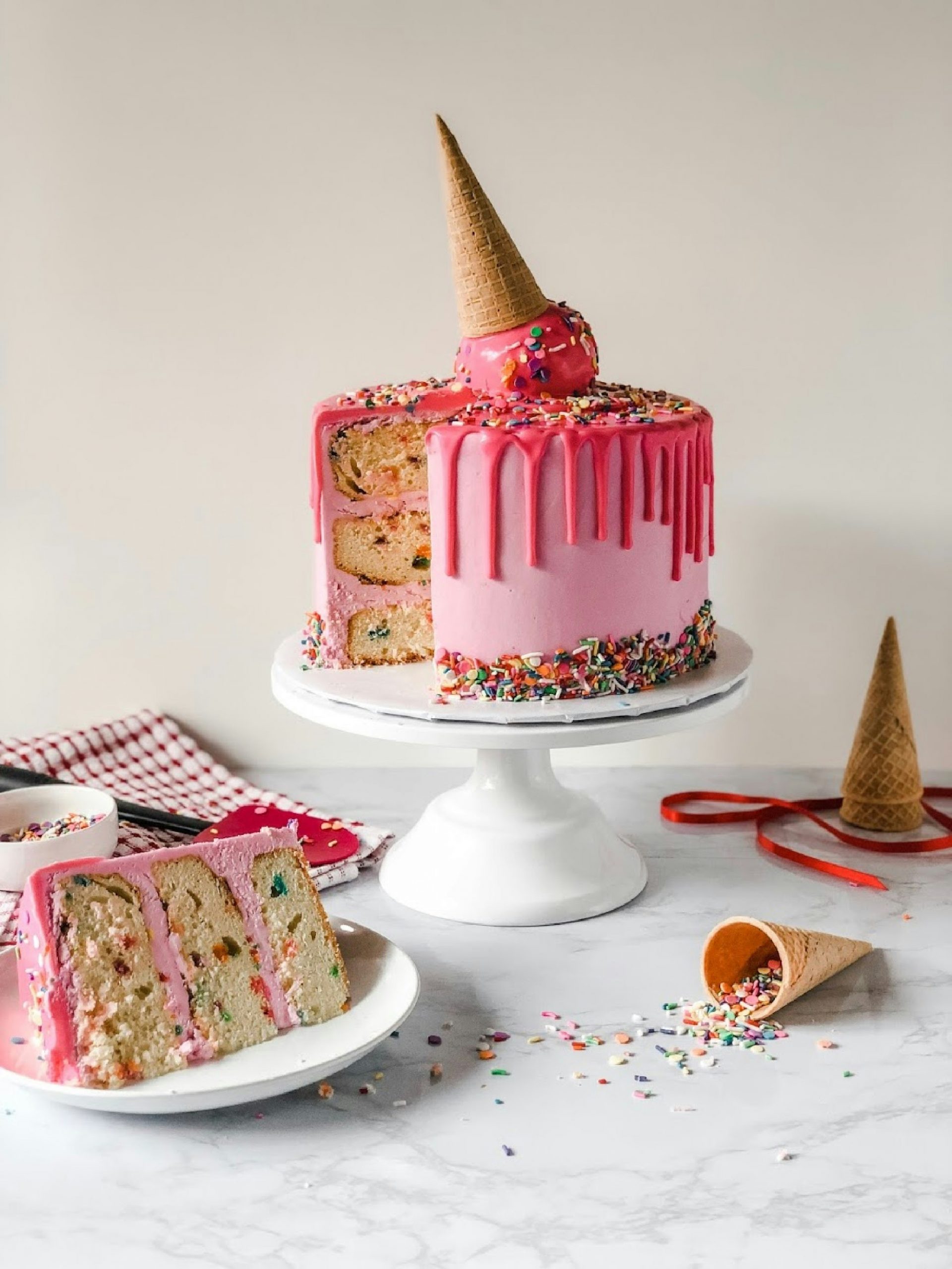 EEAT. A slice of cake on a plate, large cake on a stand with an ice cream cornet squashed into the top. Pink icing.