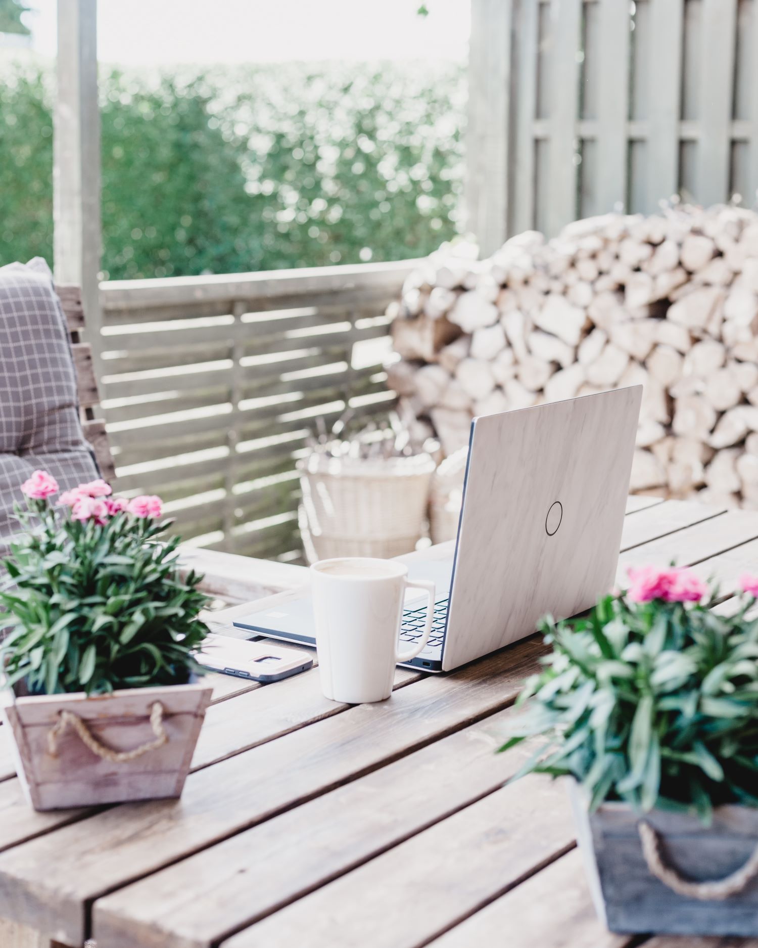 Copywriting support represented by a white table with an open laptop, two flower pots and a cup. A window in the background showing flowers