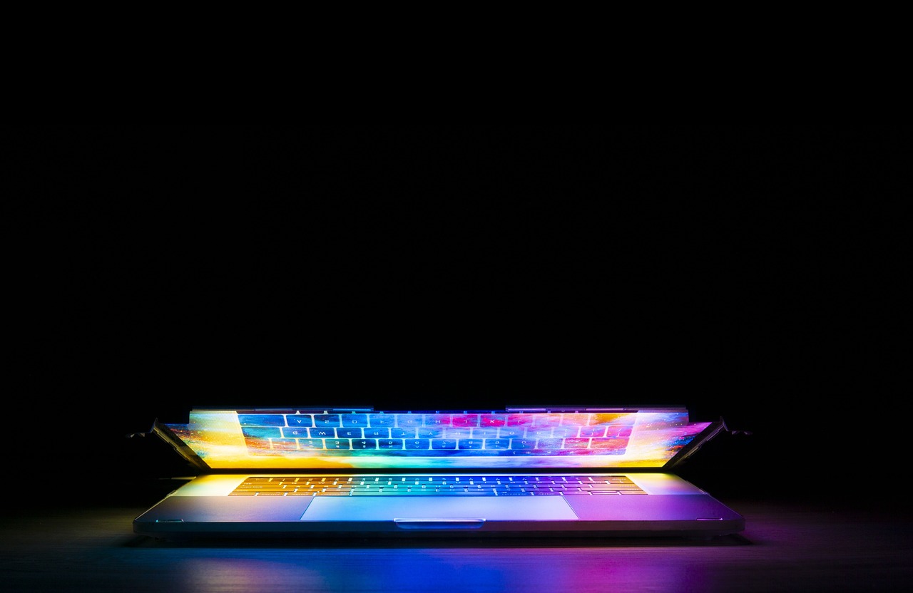 Half open laptop with multicoloured image shining against a black background