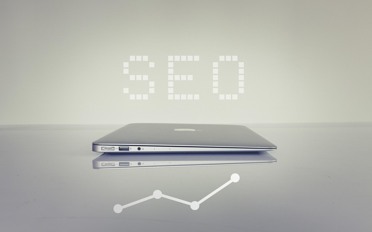 The letters SEO above a closed siler laptop with a graph line heading upwards underneath
