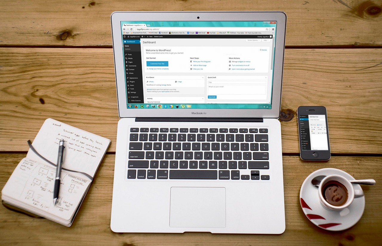 Ariel view of an open laptop with a WordPress website open on the screen, a notepad and pen, phone and cup of coffee beside it