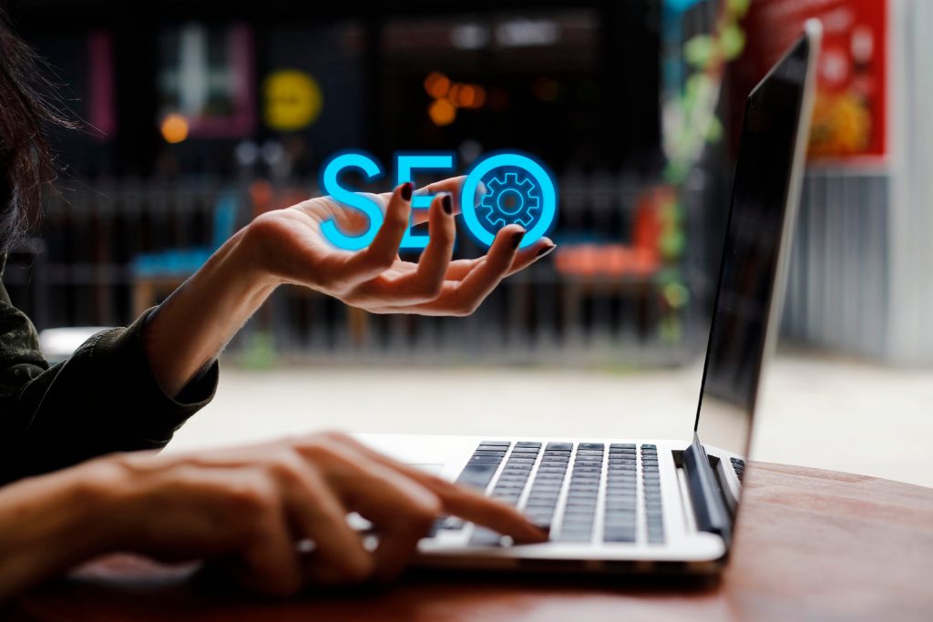 A woman holding the letters SEO with one hand, typing on a laptop keyboard with the other