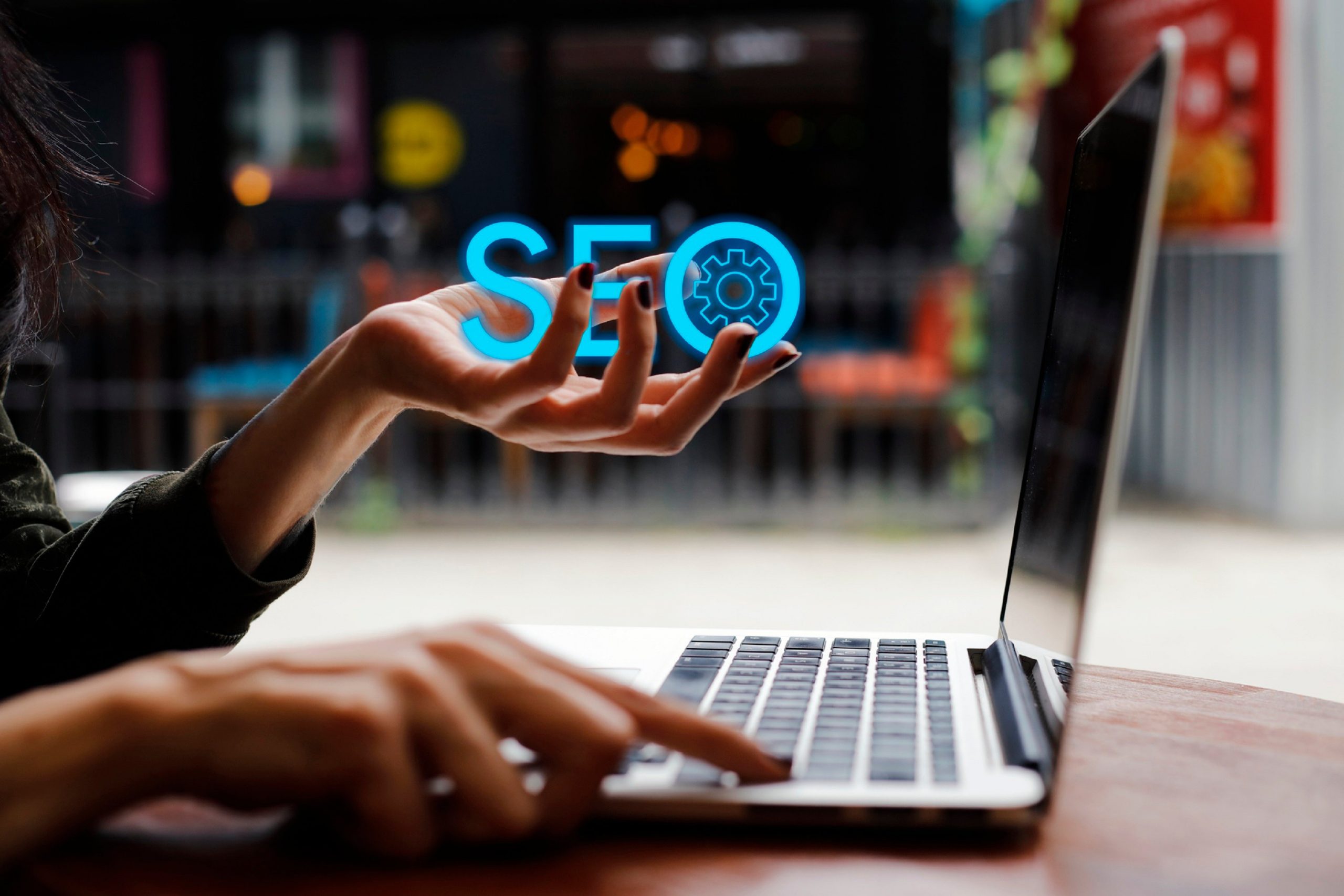 A woman holding the letters SEO with one hand, typing on a laptop keyboard with the other