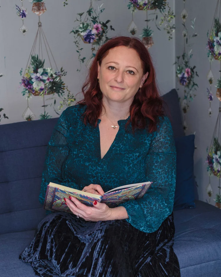 Headshot of Jenny Holliday, the Career Happiness coach, wearing a turquoise dress sitting and a settee holding an open notebook and pen